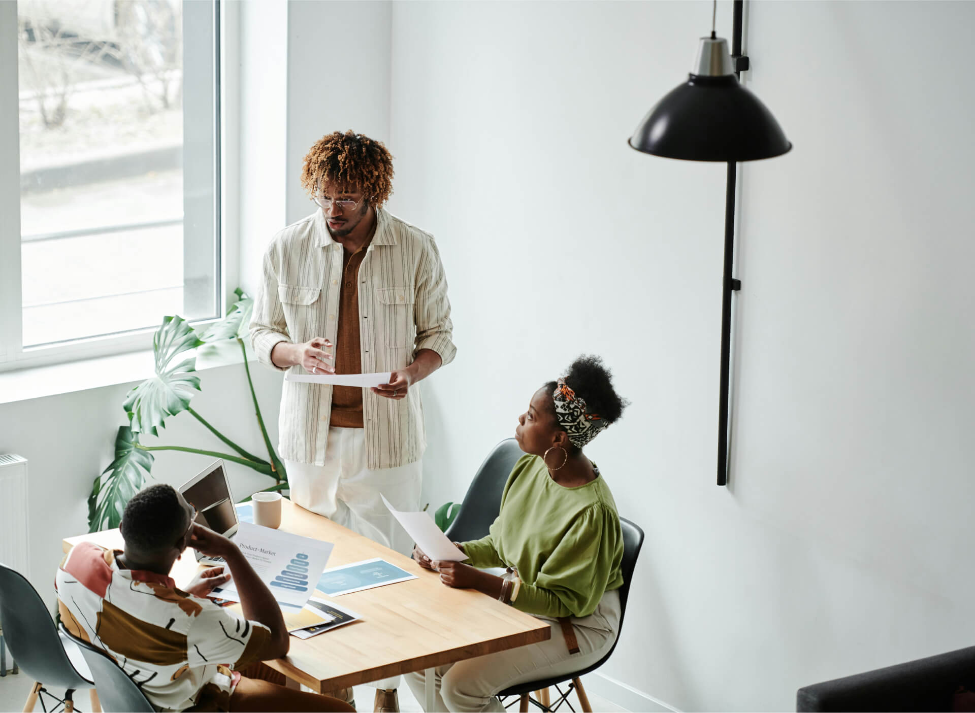 Three colleagues discussing printed documents around a table in a bright office, image from the Attic website