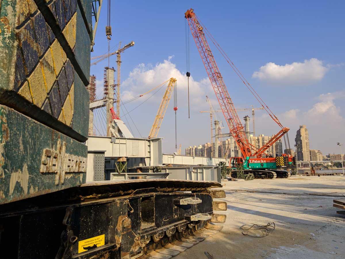 Red crawler crane lifting steel bridge sections on a construction site, from the MPS project gallery