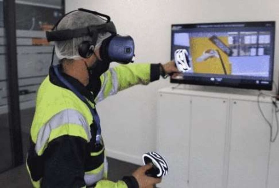 Awan 2 Trainee in a hi-vis vest using a VR headset and controllers in front of a screen
